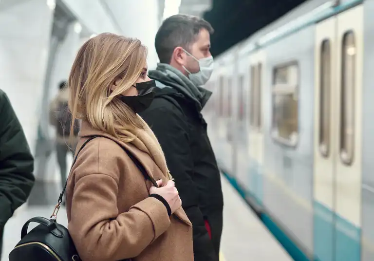 Side view of young man and woman in medical masks standing near carriage in subway